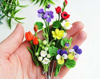 May include: A set of six handmade polymer clay flower pins. The pins feature a variety of flowers, including red tulips, yellow daffodils, white lilies of the valley, purple pansies, and a red poppy.