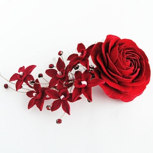 May include: A red fabric rose with a cluster of red fabric flowers and gold accents. The flowers are arranged on a comb.
