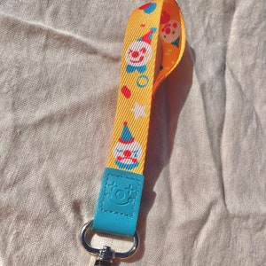 May include: A yellow lanyard with a blue and red clown pattern and a silver clip. The lanyard has a blue leather tag with the text "dot dot" on it.