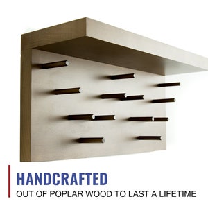 May include: A handcrafted wooden wall shelf with a light brown finish and a top shelf. The shelf has a grid of small wooden pegs for hanging items. The text "HANDCRAFTED OUT OF POPLAR WOOD TO LAST A LIFETIME" is printed below the shelf.