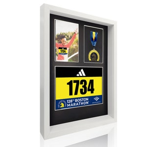 May include: A white picture frame with a black mat and three openings. The top opening contains a photo of a woman running a marathon. The middle opening contains a medal. The bottom opening contains a yellow and black marathon bib with the number 1734 and the text "128th Boston Marathon".