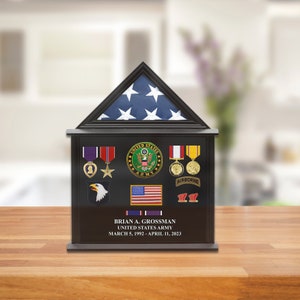May include: A black wooden shadow box with a folded American flag, medals, and patches. The box has a plaque with the text "BRIAN A. GROSSMAN UNITED STATES ARMY MARCH 5, 1992 - APRIL 11, 2023".