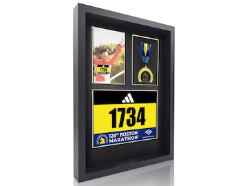 May include: Black framed display featuring a photo, a medal, and a race bib. The race bib is yellow with the number 1734 and the text "128th Boston Marathon". The medal has a blue ribbon. The photo shows a runner.