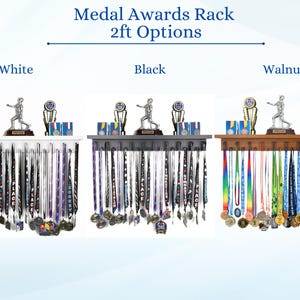 May include: Medal display racks in white, black, and walnut. Each rack holds medals and features a shelf with trophies and a figurine. The text "Medal Awards Rack 2ft Options" is at the top.