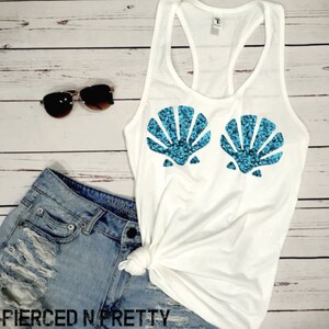 May include: White racerback tank top with two turquoise sequined seashell designs. The tank top is paired with denim shorts and sunglasses. The text "PIERCED N PRETTY" is at the bottom of the image.