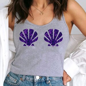 May include: A grey racerback tank top with a purple glitter seashell design. The tank top is worn with blue jeans and a white button-down shirt. The text on the bottom of the image reads: GREY RACERBACK, DESIGN: PURPLE GLITTER.