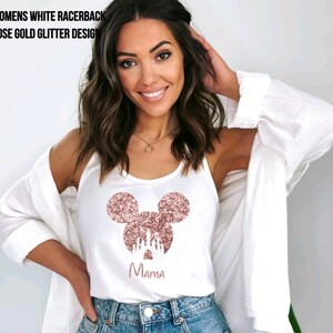 May include: White tank top with a rose gold glitter Mickey Mouse design and the word "Mama" underneath. The Mickey Mouse design features a silhouette of Cinderella's castle inside the ears.