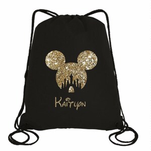 May include: Black drawstring bag with a gold glitter Mickey Mouse silhouette and the Disney castle inside the ears. The name "Kaitlyn" is written in gold glitter below the silhouette.
