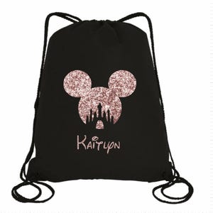 May include: Black drawstring bag with a rose gold glitter Mickey Mouse head and a castle silhouette. The bag has the name "Kaitlyn" printed below the image.