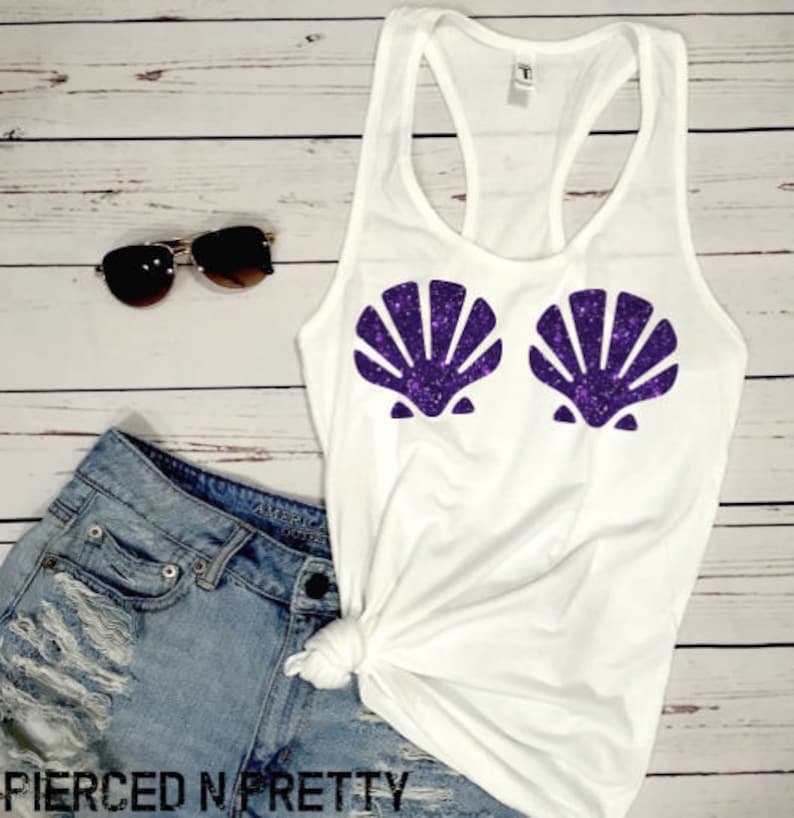 May include: White tank top with a racerback design, featuring two purple glitter seashell designs. The image also includes denim shorts, sunglasses, and the text "PIERCED N PRETTY" at the bottom.