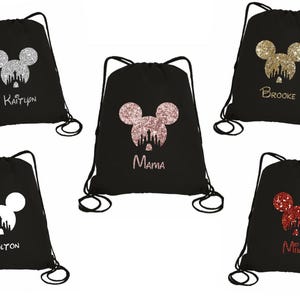 May include: Six black drawstring bags with different glitter Mickey Mouse designs and names. The names are Kaitlyn, Brooke, Mama, Colton, Mike.