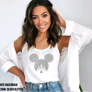 May include: White racerback tank top with a silver glitter Mickey Mouse head design featuring the Cinderella Castle inside the ears. The text "WHITE RACERBACK" and "DESIGN: SILVER GLITTER" is printed below the image.