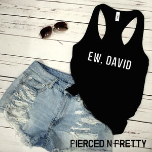 May include: A black tank top with the text "EW, DAVID" in white, paired with light blue denim shorts and sunglasses. The shorts have distressed details. The image is on a light wood background.