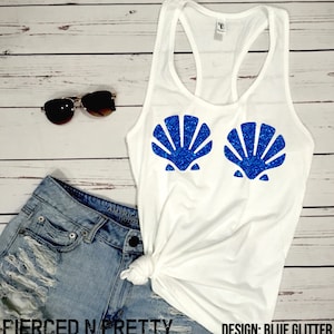 May include: White tank top with a racerback design. The shirt features two blue glitter seashell designs on the front. Sunglasses and denim shorts are also visible. The text "Pierced N Pretty" and "Design: Blue Glitter" are printed on the bottom.