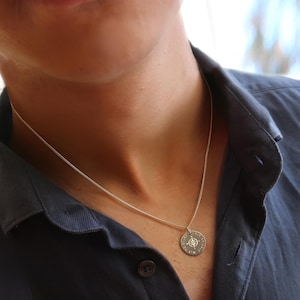 Ein Mann trägt Kompass-Kette aus 925 Silber mit Koordinaten-Gravur. Der Anhänger ist rund.