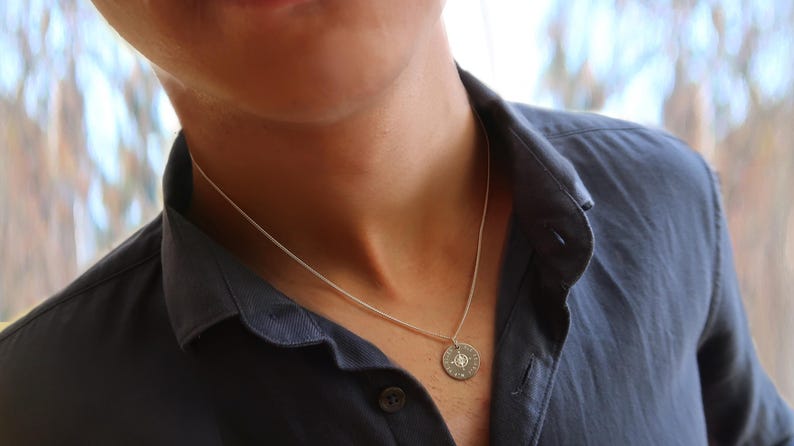 Ein Mann trägt Kompass-Kette aus 925 Silber mit Koordinaten-Gravur. Der Anhänger ist rund.