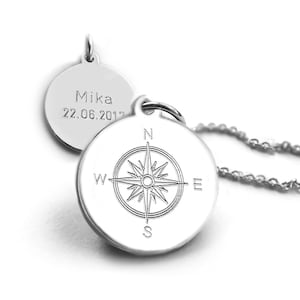 Könnte beinhalten: Eine silberne Halskette mit Anhänger, bestehend aus zwei runden Charms. Einer zeigt eine Windrose, der andere ist mit dem Namen "Mika" und dem Datum "22.06.2017" graviert. Die Halskette hat eine feine Kette.