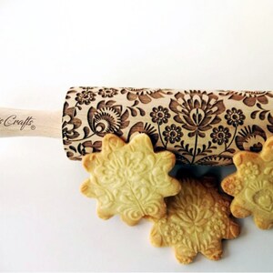 Può includere: Un mattarello di legno con un motivo floreale e la scritta "Algis Crafts" sul manico. Tre biscotti a forma di stella con disegni floreali in rilievo sono accanto al mattarello. Su sfondo bianco.