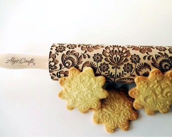 May include: A wooden rolling pin with a floral pattern and the text "Algis Crafts" on the handle. Three star-shaped cookies with embossed floral designs are next to the rolling pin. The rolling pin and cookies are on a white background.
