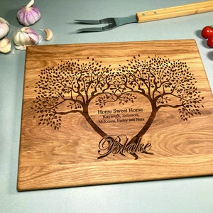 Könnte beinhalten: Ein Schneidebrett aus Holz mit einem herzförmigen Design, das zwei Bäume mit ineinander verschlungenen Ästen zeigt. Das Herz enthält den Text "Home Sweet Home, Kayleigh, Jameson, McKenna, Finley und Nora". Unter dem Herzen steht der Name "Blake".