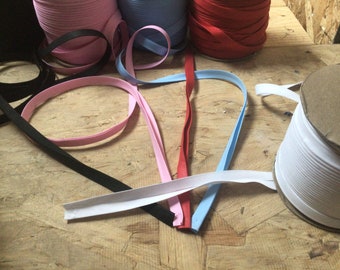 May include: Assortment of colorful bias tape in pink, black, red, blue, and white. The tape is rolled up on spools and laid out on a wooden surface.