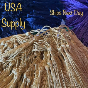 May include: A close-up image of a pile of gold tassel cords. The cords are made of a soft, silky material and have a small tassel at the end. The cords are arranged in a random pattern, creating a textured and visually appealing image.  The text "Ships Next Day" is visible in the background.
