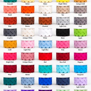 May include: A collection of 1-1/2 inch jumbo ric rac trim spools arranged in a grid. Each spool features a distinct solid color, including shades of green, yellow, orange, pink, blue, purple, red, brown, grey, and white, with labels below each.