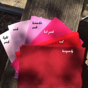 Pu&ograve; includere: Una collezione di campioni di tessuto in varie tonalit&agrave; di rosa e rosso, tra cui rosa chiaro, rosa, rosa lavanda, rosa acceso, rosso e bordeaux.