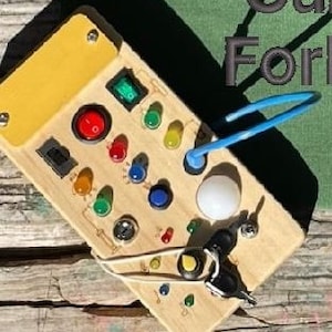 May include: Wooden toy with a variety of buttons, switches, and keys. The toy has a yellow, red, green, blue, and white color scheme. The toy is on a wooden surface.