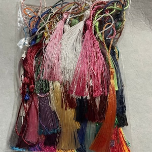 May include: A plastic bag filled with a variety of colorful tassels. The tassels are made of different materials, including silk and cotton. They are all about 2 inches long and have a variety of colors, including red, blue, green, yellow, and purple.