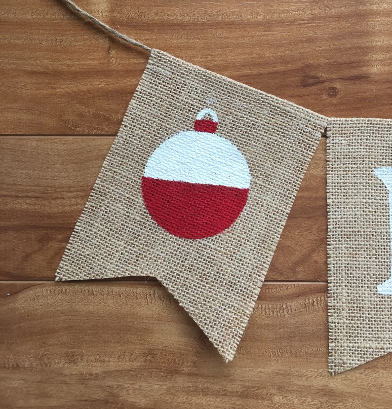 Peut inclure: Une banni&egrave;re en toile de jute avec un flotteur de p&ecirc;che rouge et blanc peint dessus. La banni&egrave;re fait partie d'une banni&egrave;re plus grande qui dit "Fish On".