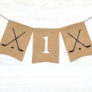 May include: A burlap banner with the number "1" in the center and hockey stick graphics on either side. The banner is strung on twine.