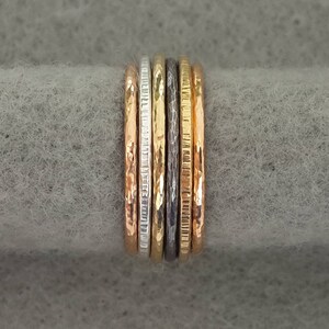 May include: A set of five thin gold, silver, and black rings stacked together. The rings have different textures, including hammered, smooth, and textured.