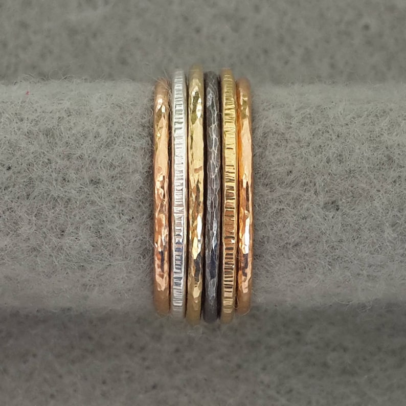 May include: A set of five thin gold, silver, and black rings stacked together. The rings have different textures, including hammered, smooth, and textured.