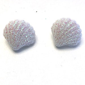 May include: Two white seashell-shaped decorative items with iridescent glitter accents. The shells have a textured surface and a scalloped edge. These decorative items are perfect for craft projects or coastal-themed decor.