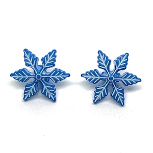 May include: A pair of snowflake-shaped earrings. Each earring is a vibrant blue with white leaf-like details, creating a contrasting design. The earrings are set against a white background, highlighting their intricate design.