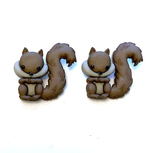 May include: Two brown squirrel-shaped embellishments with fluffy tails and light tan accents. The squirrels have a light tan chest and a white collar. The embellishments are on a white background.