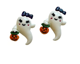 May include: A pair of Halloween-themed earrings featuring white ghost figures with black bows and holding orange pumpkin-shaped treat buckets. The ghosts have rosy cheeks and smiling faces, perfect for the spooky season.