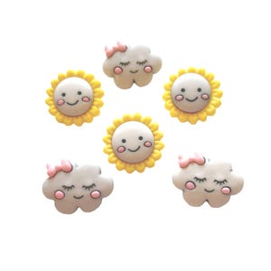 May include: Six whimsical embellishments: three smiling suns with yellow petals and three sleeping cloud shapes with pink bows. The suns and clouds have smiling faces and are set against a white background.