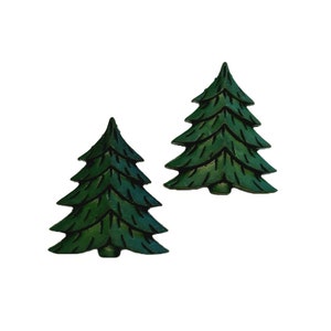 May include: Two dark green, stylized Christmas tree ornaments. Each tree has multiple layers of branches and a pointed top. The ornaments are set against a white background.
