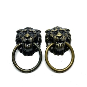 May include: Two antique-style lion head door knockers with bronze finish. Each knocker features a detailed lion's face with a ring-shaped handle. The knockers are made of metal and are designed for doors.