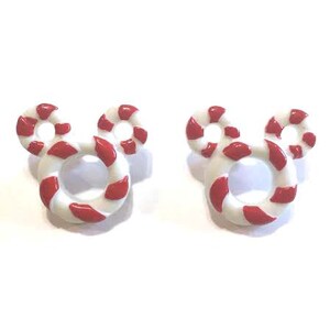 May include: Pair of white and red candy cane-striped Mickey Mouse-shaped earrings. The earrings have a circular design with red stripes on a white background. The earrings are a festive accessory.