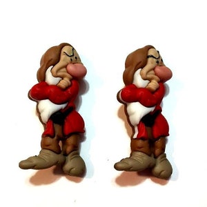 May include: Two resin figurines of Grumpy from Snow White. Each figure is depicted with a brown head, a white beard, a red coat, and brown pants. The figures are standing with their arms crossed.