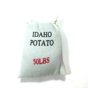 May include: A small, white fabric sack with the words "IDAHO POTATO" in black and "50 LBS" in red. The sack is tied at the top with a white string.