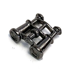 May include: A small, dark gray metal object with a geometric design. The object appears to be a decorative element, possibly for jewelry or crafts. The design consists of several cylindrical shapes connected by bars, creating a lattice-like structure.