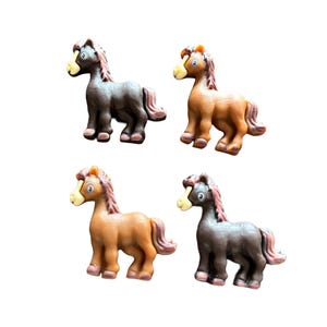 May include: Four small horse figurines in shades of brown and gray are arranged against a white background. Each horse has a light-colored muzzle, a pink mane and tail, and is in a standing position.