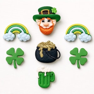 May include: A collection of seven decorative buttons featuring a leprechaun head, two rainbows, two four-leaf clovers, a black pot filled with gold glitter, and a green beer mug with white foam. Each button has a distinct shape and color.