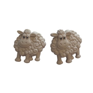May include: Two off-white sheep figurines. Each sheep has a curly wool coat, four legs, and a smiling face with large eyes. The sheep are standing upright, facing forward, and are set against a white background.