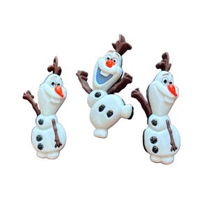 May include: Three white snowman figurines with black button details, brown twig arms, and carrot noses. The snowmen have brown twig hair and are smiling. The background is white.