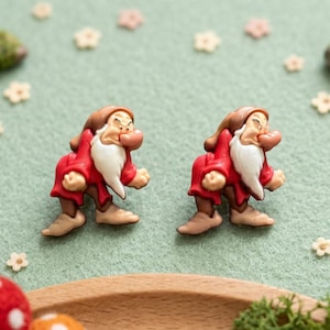 May include: A pair of Grumpy dwarf character buttons featuring a red tunic, brown hat, and white beard. Each button depicts the character with a furrowed brow and crossed arms, rendered in a detailed, molded design with a smooth, glossy finish.